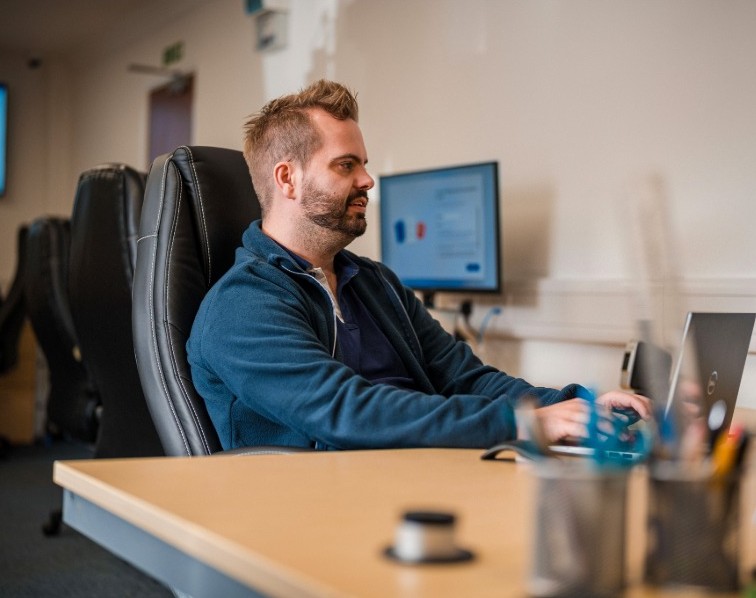IT support professional working at a desk, monitoring systems and providing proactive managed IT services using a laptop and desktop displays.