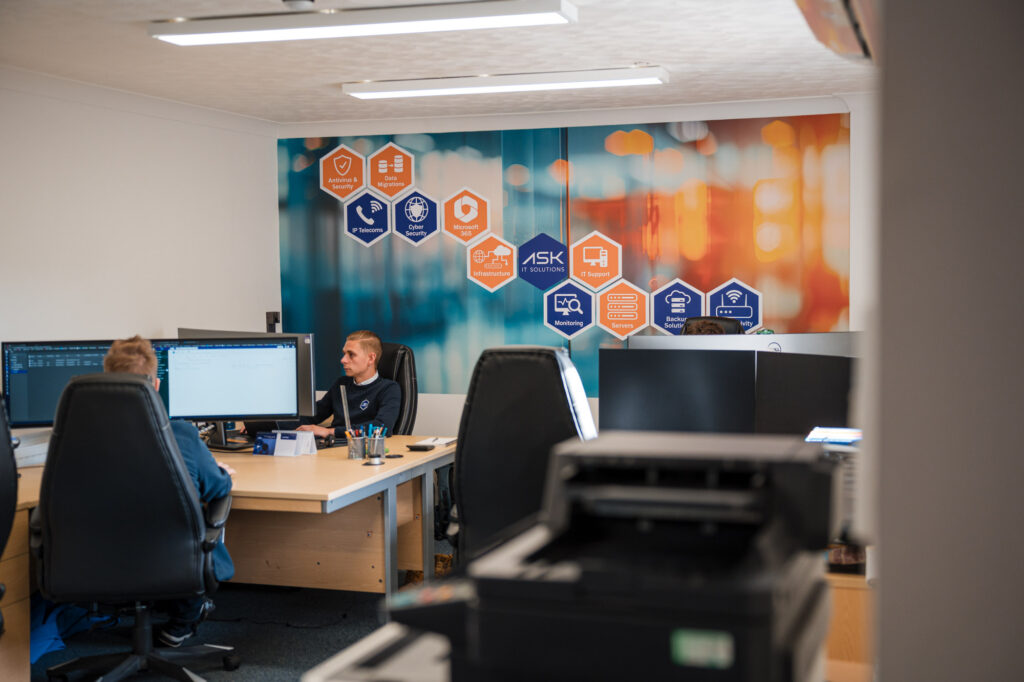 Microsoft 365 support and management. Modern IT services office with team members working at computer workstations, providing Microsoft 365 management, technical support and business technology services.